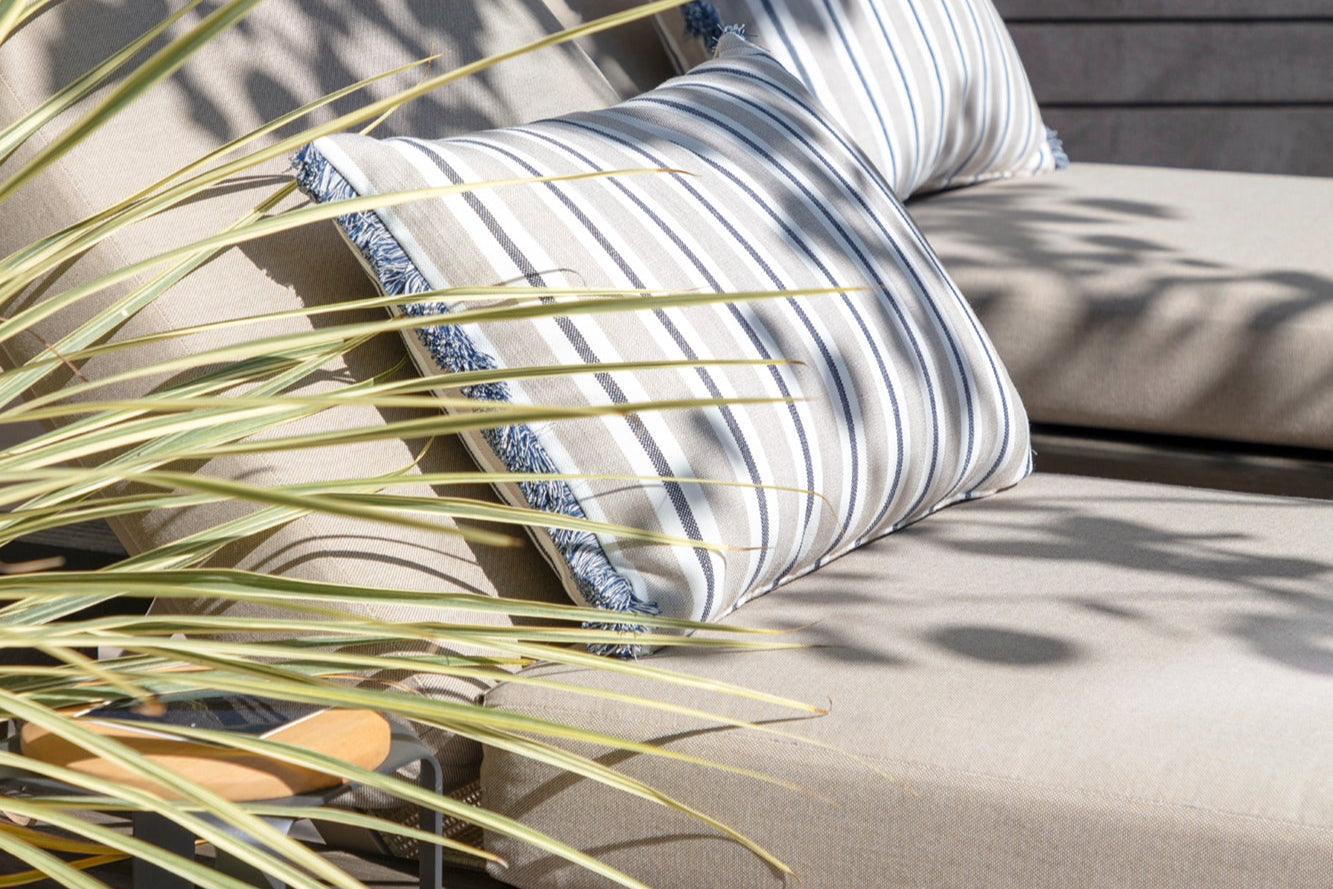 Striped pillow on a beige outdoor sofa with a plant in the foreground