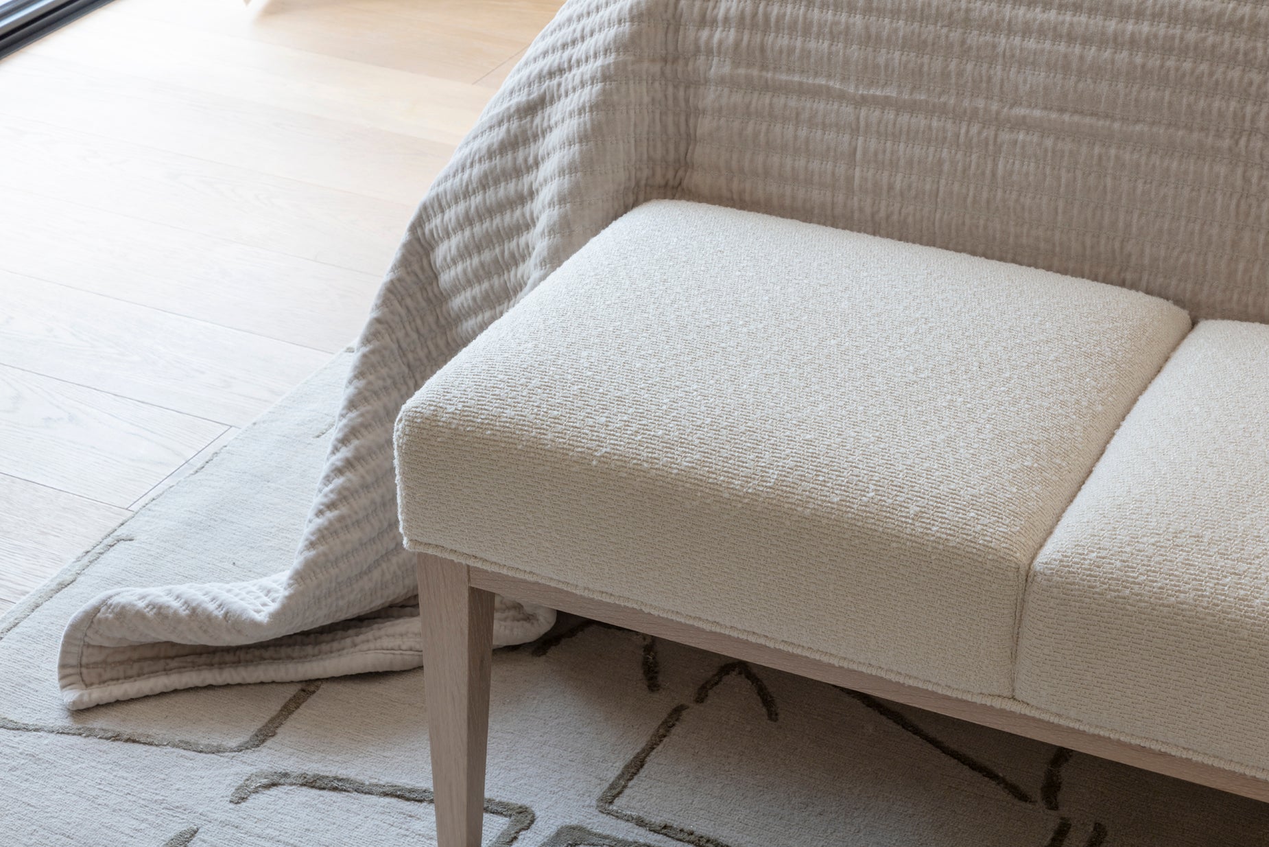 Cream textured bed footer with rustic wooden legs, luxury bespoke patterned rug and handmade throw by Nineteen Interiors.