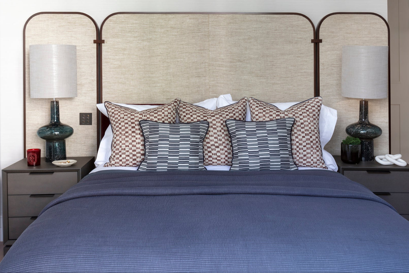 Bedroom with a bed featuring blue bedding and patterned pillows, flanked by nightstands with lamps.
