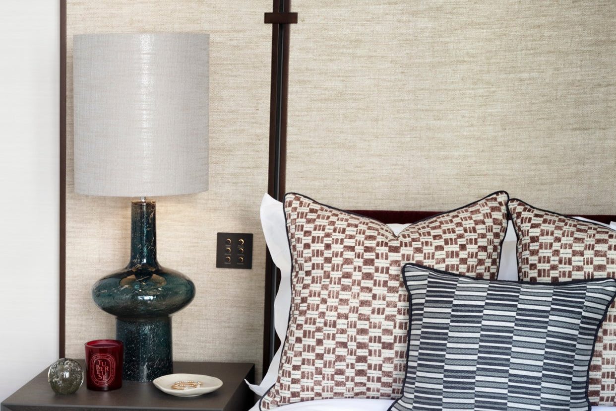 Decorative pillows on a bed with a lamp and nightstand in the background.