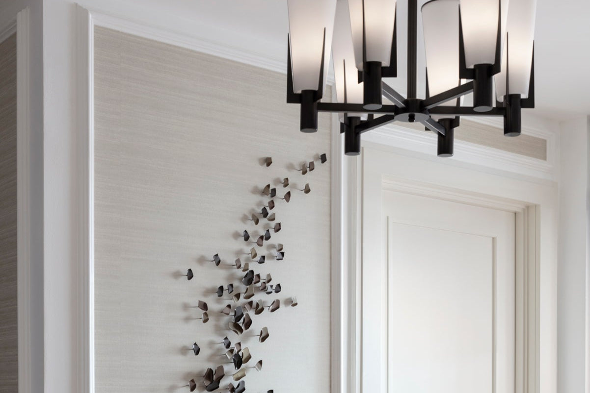 Modern chandelier hanging adjacent to handmade peddle and leaf sculpture, surrounded by bespoke wall panelling and feature lighting