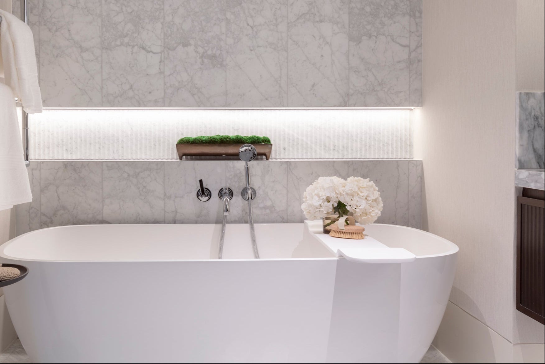 Modern Free Standing Bathtub with stone feature wall, silver ironmongery, faux flowers and accessories by Nineteen Interiors.