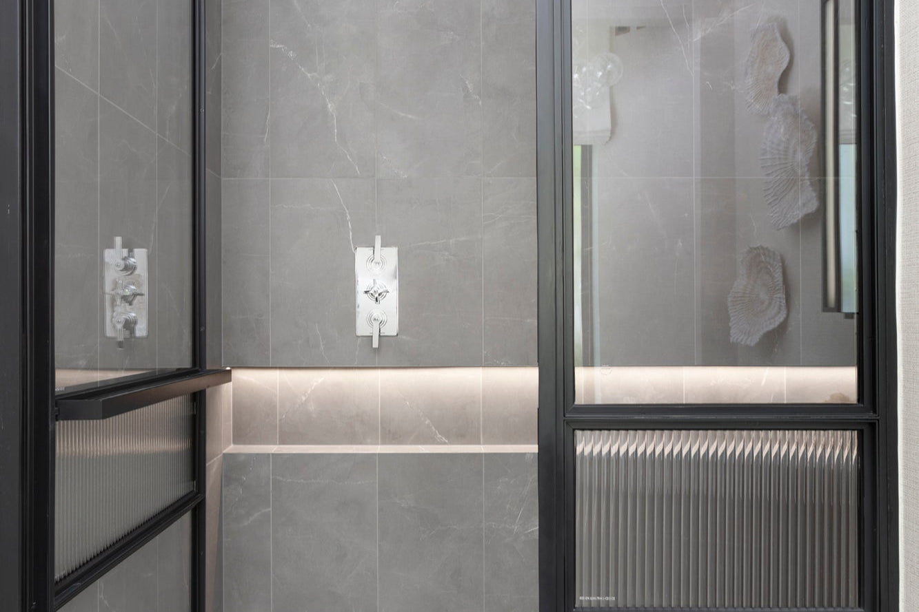 Bathroom with gray tiled walls and a glass shower enclosure.