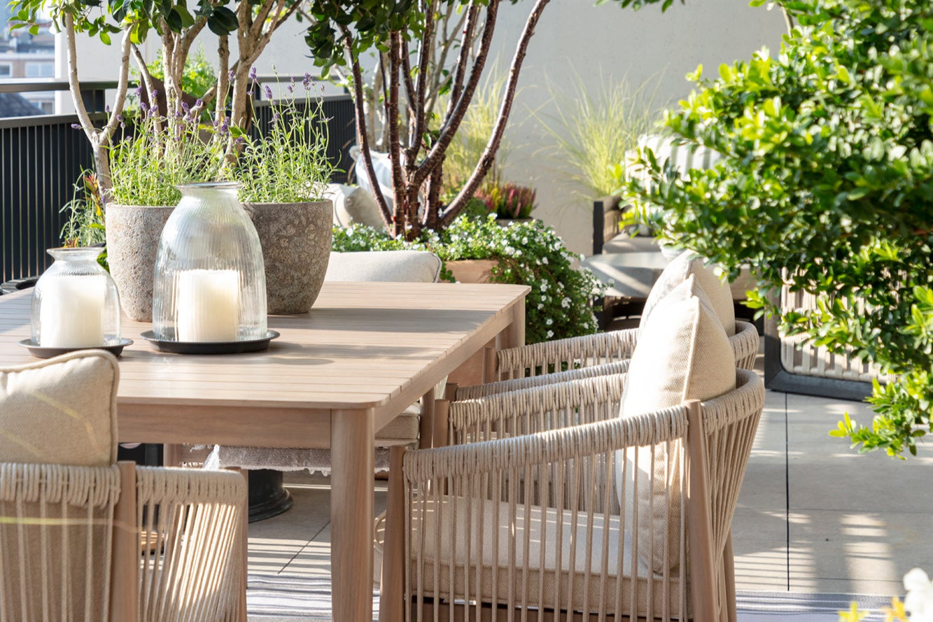 Outdoor patio dining setting with wooden table and chairs, surrounded by potted plants, glass lantern accessories by Nineteen Interiors.