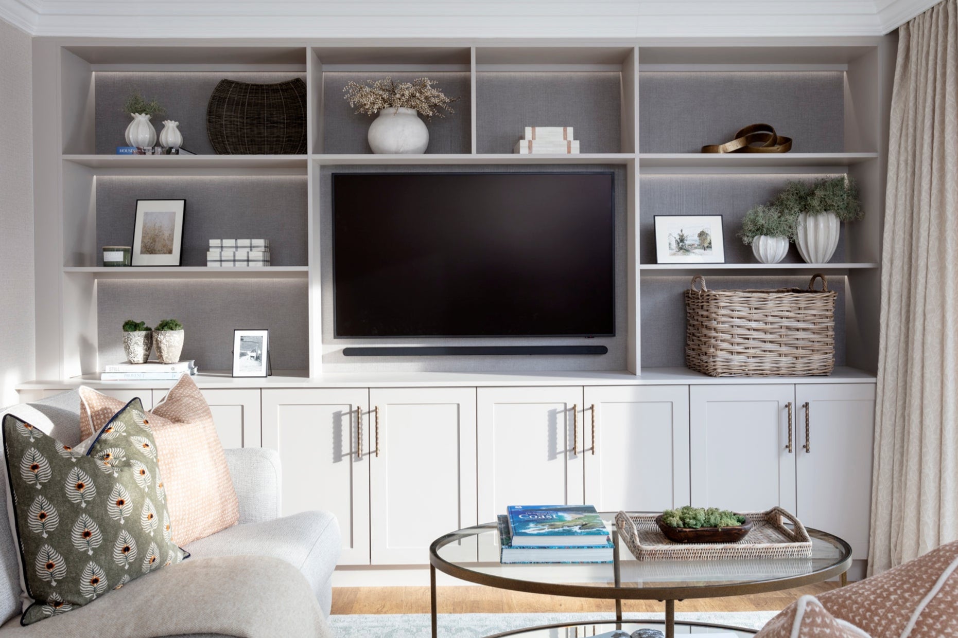 Glass coffee table with luxury coffee table books, a display tray, and a fabric throw, paired with a wall-to-wall joinery unit. The space is enhanced with interior design accessories and moss, creating a sophisticated, modern living room atmosphere