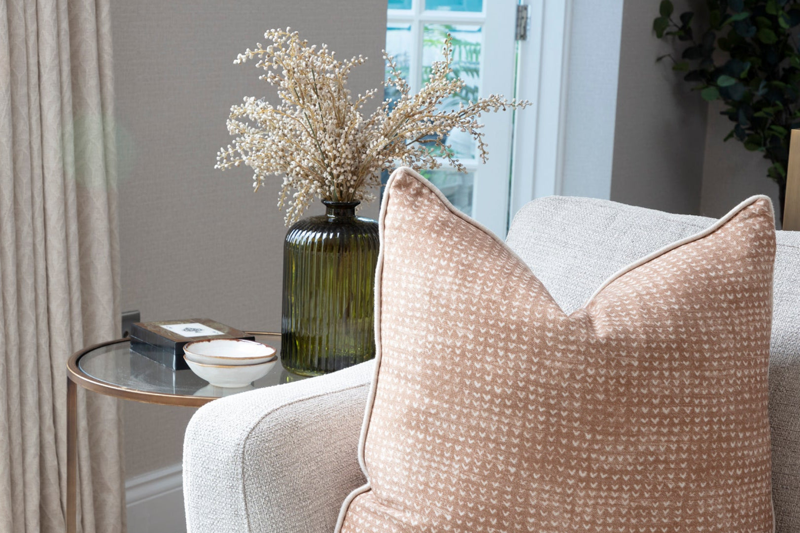 Glass side table, neutral high-end sofa with bespoke cushions, handmade and made-to-measure curtains, and wooden flooring in a French-inspired family lounge in Buckinghamshire. The space features elegant glassware and a welcoming, sophisticated atmosphere perfect for family gatherings