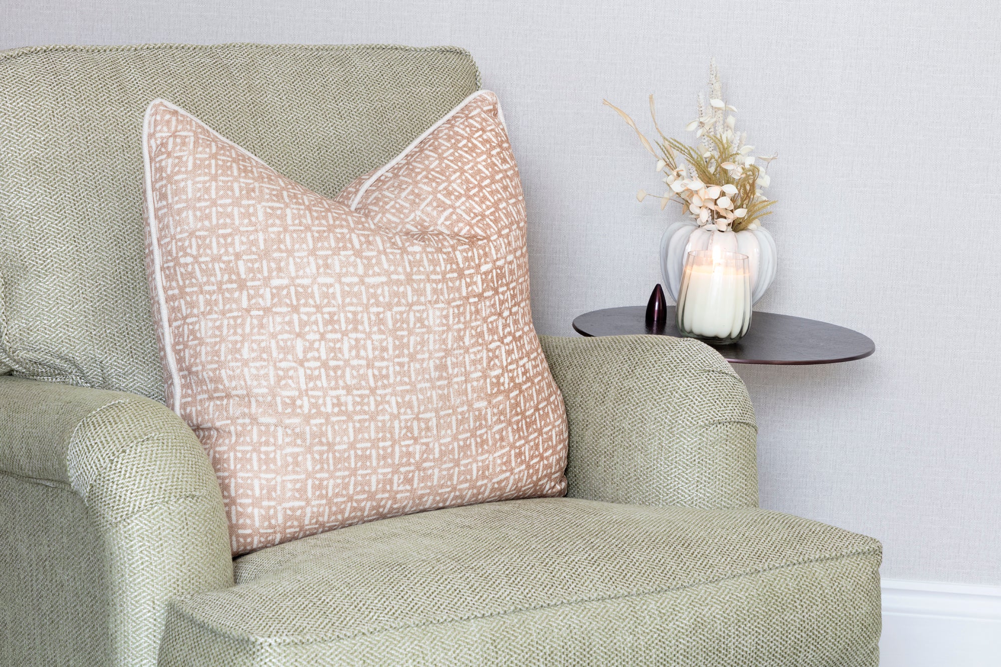 Green fabric armchair with a brass side table for reading and relaxing, accompanied by a handmade candle and a stone vase with flowers. In the background, beautiful wallpaper, new skirting, and wooden flooring create an elegant breakout space at the back of a family lounge, offering a cosy and stylish retreat